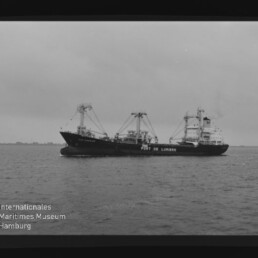 Frachtschiff Port de Lumière auf ruhiger See, Schwarzweiß-Aufnahme mit sichtbarem Filmrand und Museumslogo.