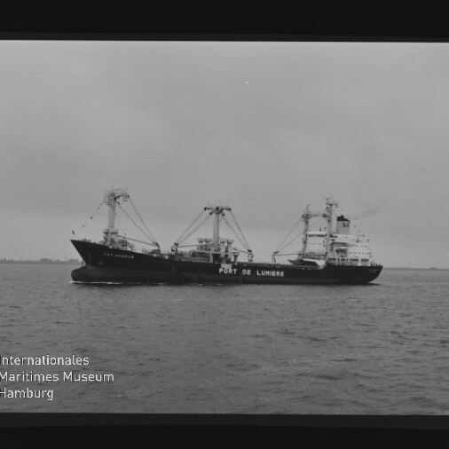 Schwarzweißaufnahme des Frachtschiffs Port de Lumière mit Ladekränen auf ruhiger See.