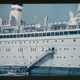 Passagierschiff mit Gangway und Rettungsbooten, kleine Barkasse am Wasser und Logo des Maritimen Museums Hamburg.