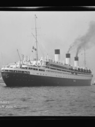 Großer vintage Ozeandampfer mit drei rauchenden Schornsteinen, begleitet von einem Schlepper vor einem Hafen.