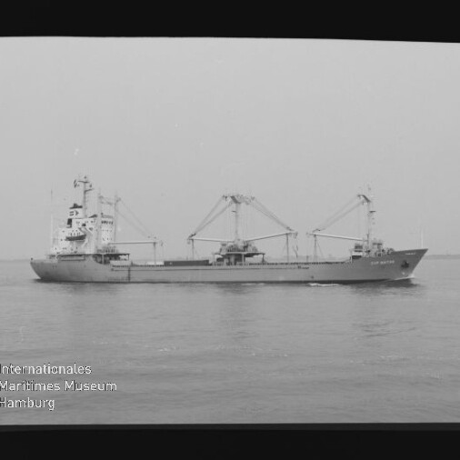 Seitliche Ansicht eines Frachtschiffs mit drei Ladekränen auf ruhiger See, schwarzweiß-Fotografie mit Museumswasserzeichen