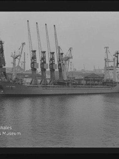 Schwarzweißfoto eines am Kai liegenden Frachtschiffs mit vier Ladekränen und dem Schriftzug Maritimes Museum Hamburg.