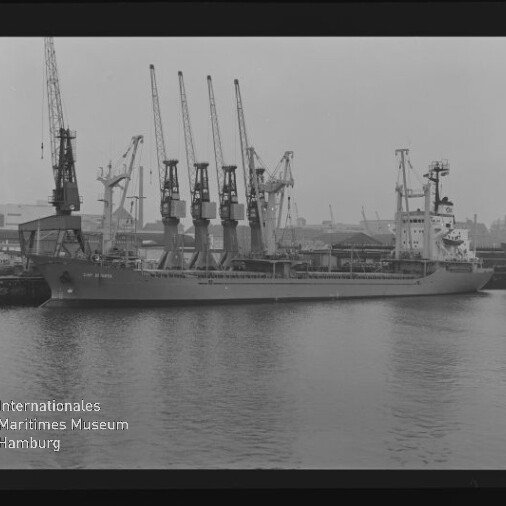 Schwarzweißfoto eines am Kai liegenden Frachtschiffs mit vier Ladekränen und dem Schriftzug Maritimes Museum Hamburg.