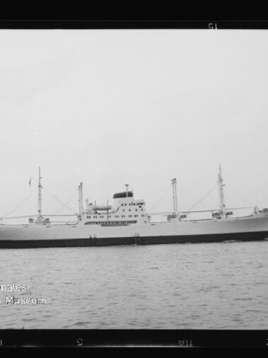 Seitliche s/w-Ansicht eines großen Frachtschiffs mit Aufbauten und Ladekränen, ruhig auf dem Wasser; Museumslogo unten links.