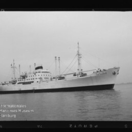 Weißes Frachtschiff mit Aufbauten und Masten auf ruhiger See, Filmrand und Wasserzeichen 