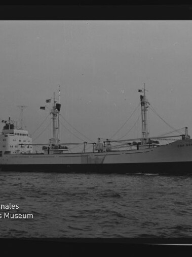 Frachtschiff mit zwei Lademasten und Brückenaufbau fährt auf ruhiger See; Museumswasserzeichen unten links.
