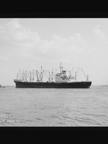 Frachtschiff mit mehreren Ladekränen auf ruhiger See, Kleinfahrzeuge am Rand; Stempel Maritimes Museum Hamburg.