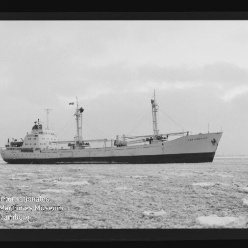 Großes Frachtschiff mit zwei Ladebäumen auf eisbedeckter See unter trübem Himmel, schwarz-weiß-Foto.