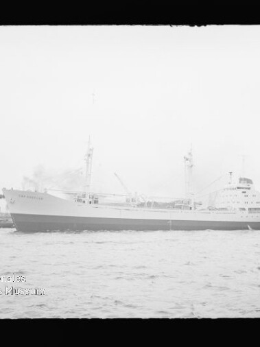 Seitliche Aufnahme eines großen Frachtschiffs vor einem Industriehafen, ruhige See in einem Schwarzweißfoto.