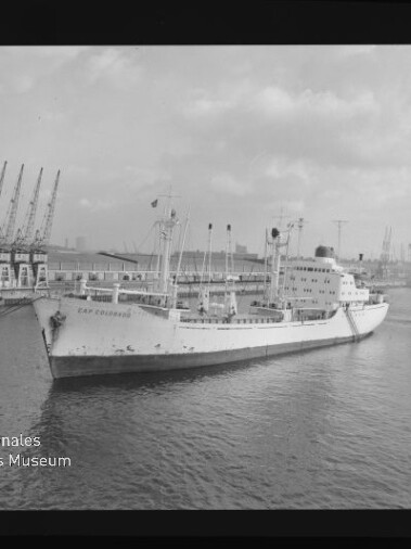 Frachtschiff Cap Colombie am Kai eines Industriehafens, mit Ladekränen und Hafenanlagen im Hintergrund.