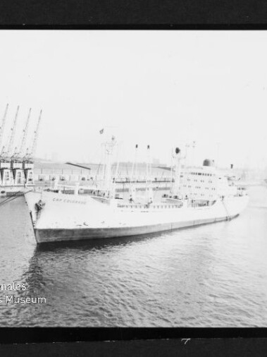 Großes weißes Schiff mit mehreren Masten und Schornstein am Kai vor Hafenkränen, Museumssiegel unten links
