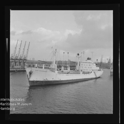 Weißes Frachtschiff im Hafen vor Kränen, unten links Logo 