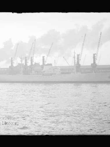 Dampfiges Schwarz-Weiß-Foto eines Frachtschiffs am Industriehafen mit Kränen im Hintergrund und einer Boje im Vordergrund.
