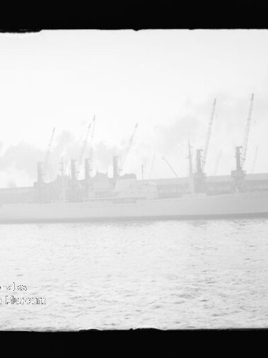 Großes Frachtschiff am Kai vor mehreren Hafenkränen, rauchige Dunststimmung und eine Boje im Vordergrund.