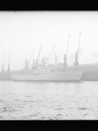Weißes Schiff am Industriehafen mit einer Reihe hoher Kräne im Nebel, Wasser im Vordergrund und Museumsstempel links unten.