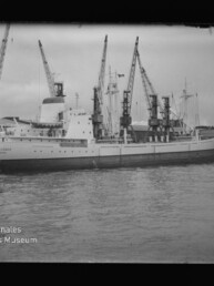 Frachtschiff am Kai unter mehreren Ladekränen in schwarzweiß; Museumslogo Maritimes Museum Hamburg unten.