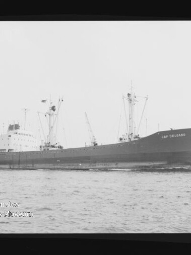 Frachtschiff Cap Delgado in Seitenansicht auf ruhiger See, mit Ladekränen und sichtbarem Schornstein.