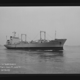 Großes Frachtschiff seitliche Ansicht auf ruhiger See, schwarzweiß mit Museumswasserzeichen unten links.