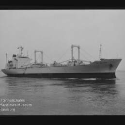 Frachtschiff mit drei Ladekränen und achternem Aufbau auf ruhigem Meer; Wasserzeichen Int. Maritimes Museum Hamburg