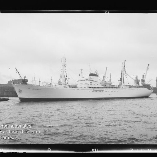 Weißes Passagierschiff im Hafen, von Kränen und Schleppern begleitet; Wasserzeichen Internationales Maritimes Museum Hamburg.