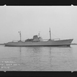 Langes Schiff mit zwei Masten und markanten Aufbauten auf ruhigem Wasser; Wasserzeichen 'Internationales Maritimes Museum Hamburg'.