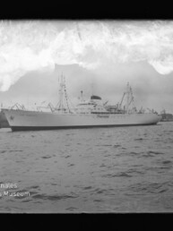 Weißes Passagierschiff im Hafen, von Schleppern begleitet, mit Hafenbebauung im Hintergrund und Museumswasserzeichen links unten.
