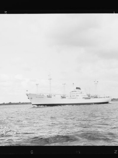 Weißes Frachtschiff mit mehreren Masten auf ruhigem Wasser vor flachem Küstenhorizont, Museumslogo unten links.
