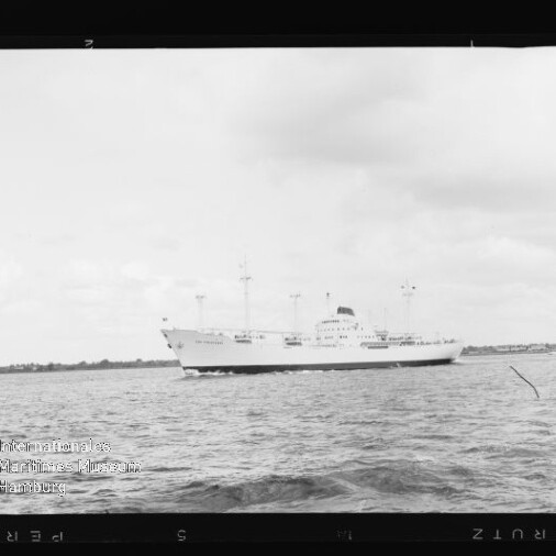 Weißes Frachtschiff mit mehreren Masten auf ruhigem Wasser vor flachem Küstenhorizont, Museumslogo unten links.