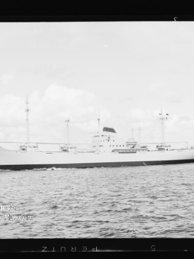 Weißes Frachtschiff mit mehreren Masten fährt auf ruhiger See, kleiner Schlepper am Heck.