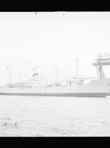 Langes weißes Passagierschiff im Hafen, neben einer Werft mit Kran und Pier sichtbar.