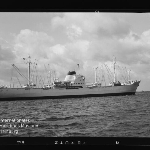 Schwarzweißfoto eines Frachtschiffs mit Ladebäumen und einem Schornstein auf ruhiger See; Museumslogo links unten