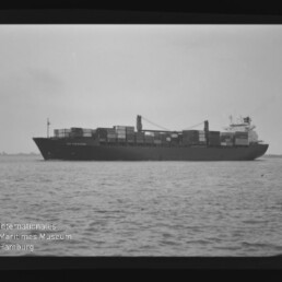 Containerschiff seitlich auf ruhiger See mit gestapelten Containern und Museumswasserzeichen unten links.
