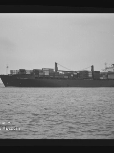 Containerschiff seitlich auf ruhiger See mit gestapelten Containern und Museumswasserzeichen unten links.