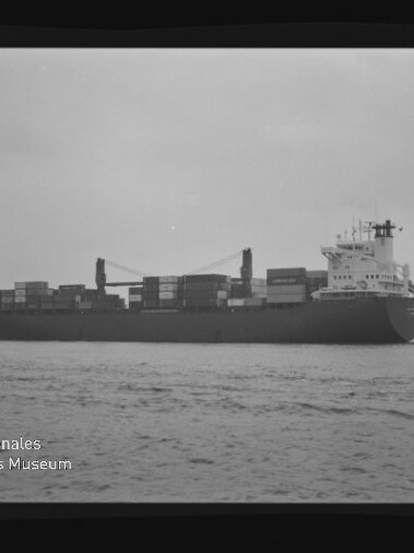 Containerschiff in Seitenansicht mit Containern und Kränen auf ruhiger See; Filmrand zeigt AGFA APX 100 und Museumslogo.