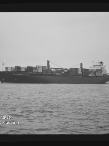 Schwarzweißaufnahme eines beladenen Containerschiffs auf ruhiger See mit gestapelten Containern, seitliche Ansicht.