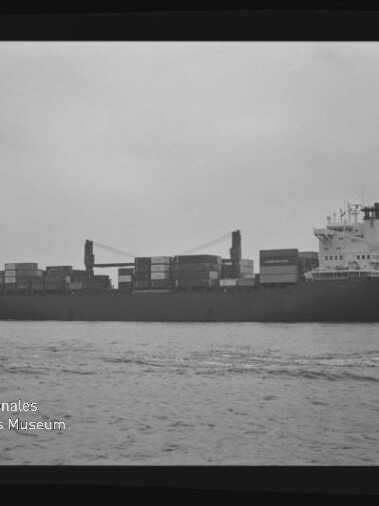 Containerschiff mit gestapelten Containern auf ruhigem Wasser, Schwarzweißaufnahme mit Museumslogo unten links.