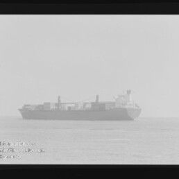 Frachtschiff mit Containern auf ruhiger See, leicht verschwommenes Schwarzweißfoto mit Filmrand und Museumslogo Internationales Maritimes Museum Hamburg