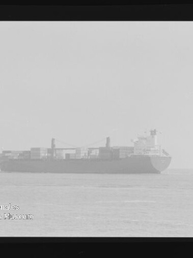Frachtschiff mit Containern auf ruhiger See, leicht verschwommenes Schwarzweißfoto mit Filmrand und Museumslogo Internationales Maritimes Museum Hamburg