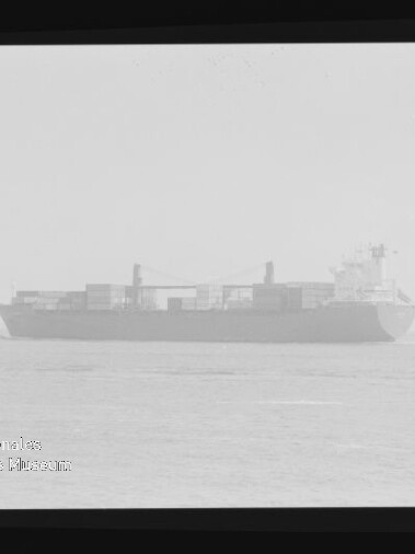 Frachtschiff mit gestapelten Containern fährt im Nebel auf ruhiger See; Filmrand und Museumswasserzeichen links unten.