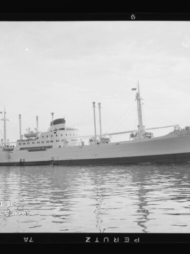 Schwarzweißes Frachtschiff mit Schornstein und Ladekränen auf ruhigem Wasser; Museumslogo unten links.