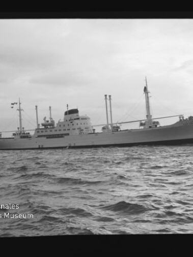 Großes Frachtschiff mit Masten und mittiger Aufbauten auf ruhiger See, links unten Wasserzeichen 