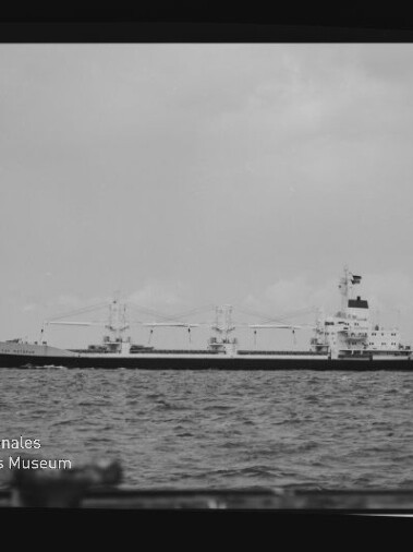 Schwarzweißaufnahme eines Frachtschiffs mit Ladekränen auf ruhiger See; unten links Stempel Internationales Maritimes Museum Hamburg.