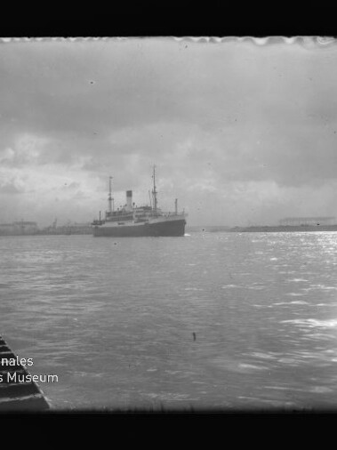 Dampfer im Hafen bei bewölktem Himmel, Pier links und Lichtreflexe auf dem Wasser; Logo des Maritimen Museums unten links.
