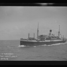 Passagierdampfer mit mittigem Schornstein und Masten fährt auf offener See, Wasserzeichen Internationales Maritimes Museum Hamburg unten links.