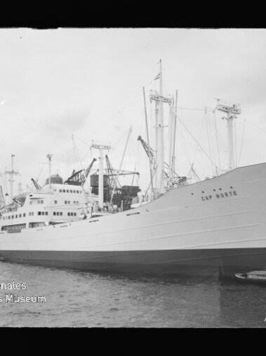 Weißes Passagier- und Frachtschiff Cap Bonnie längsseits am Kai mit Masten, Ladekränen und ruhigem Wasser.