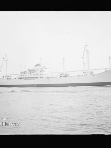 Weißes Passagier- bzw. Frachtschiff in Seitenansicht mit Masten und Signalflaggen, fahrend auf ruhigem Wasser.
