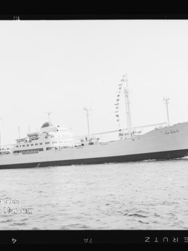 Weißes Passagierschiff mit Signalfahnen an mehreren Masten fährt über ruhige See, schwarz-weiß-Foto.
