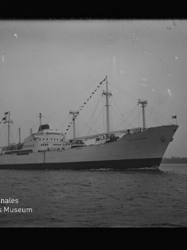 Großes Passagier- und Frachtschiff mit beflaggten Masten auf ruhigem Meer; Schwarzweißbild mit Museumslogo.