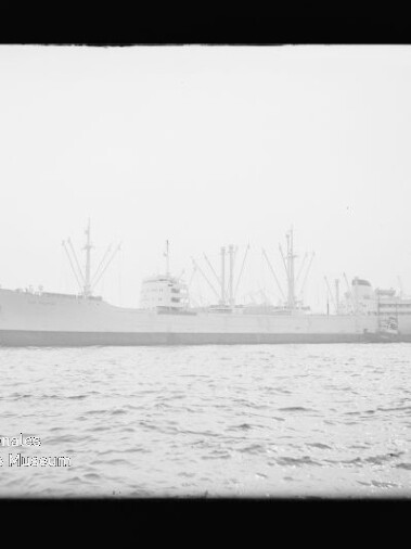 Schwarzweißaufnahme eines großen Frachtschiffs mit mehreren Ladekränen im Hafen, seitliche Ansicht auf ruhigem Wasser.