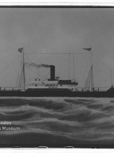 Schwarzweißaufnahme eines Dampfschiffs mit hohem Schornstein und Flaggen, fahrend auf bewegter See, Museumswasserzeichen links.